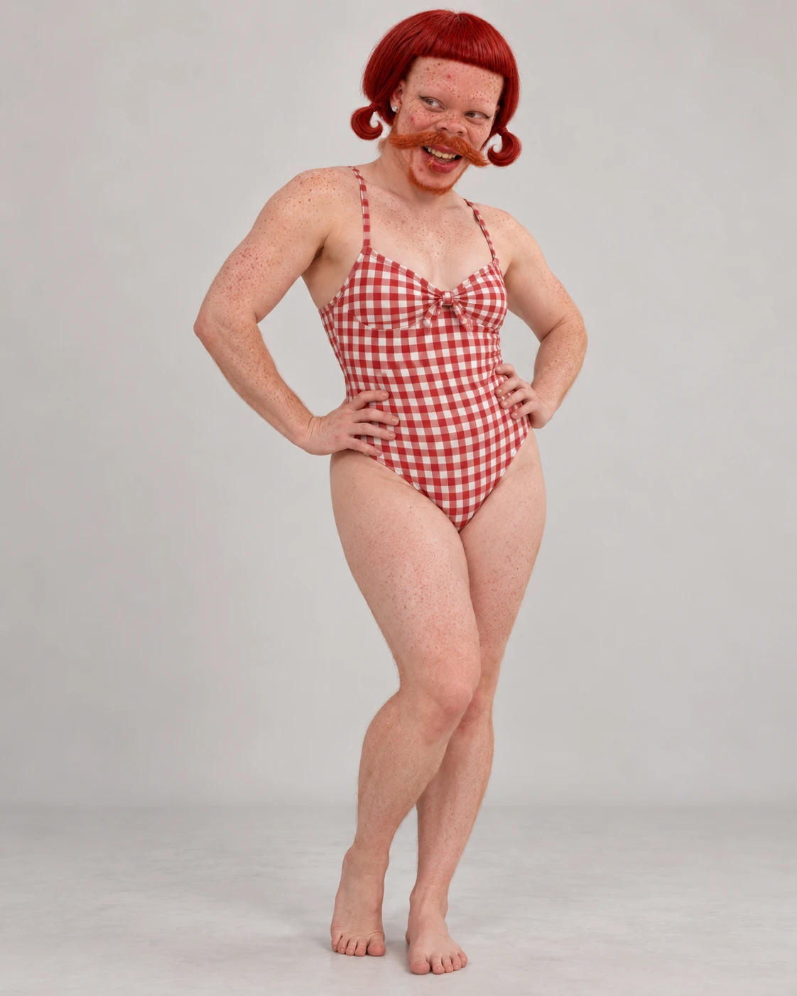 Dorothy Pudgewick standing with hands on hips in a red gingham swimsuit, red pigtails and a large ginger handlebar mustache